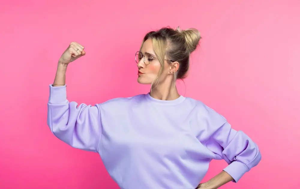Mujer levantando el brazo con confianza sobre fondo rosa